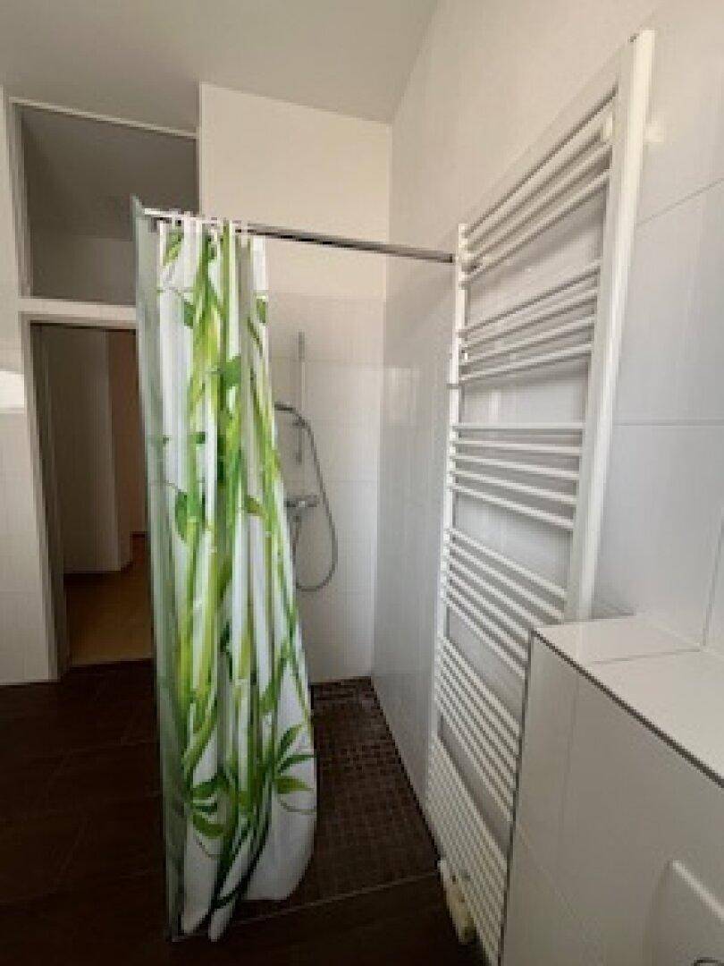 Badezimmer mit Duschbereich, beheiztem Handtuchhalter und weißen Wandfliesen.