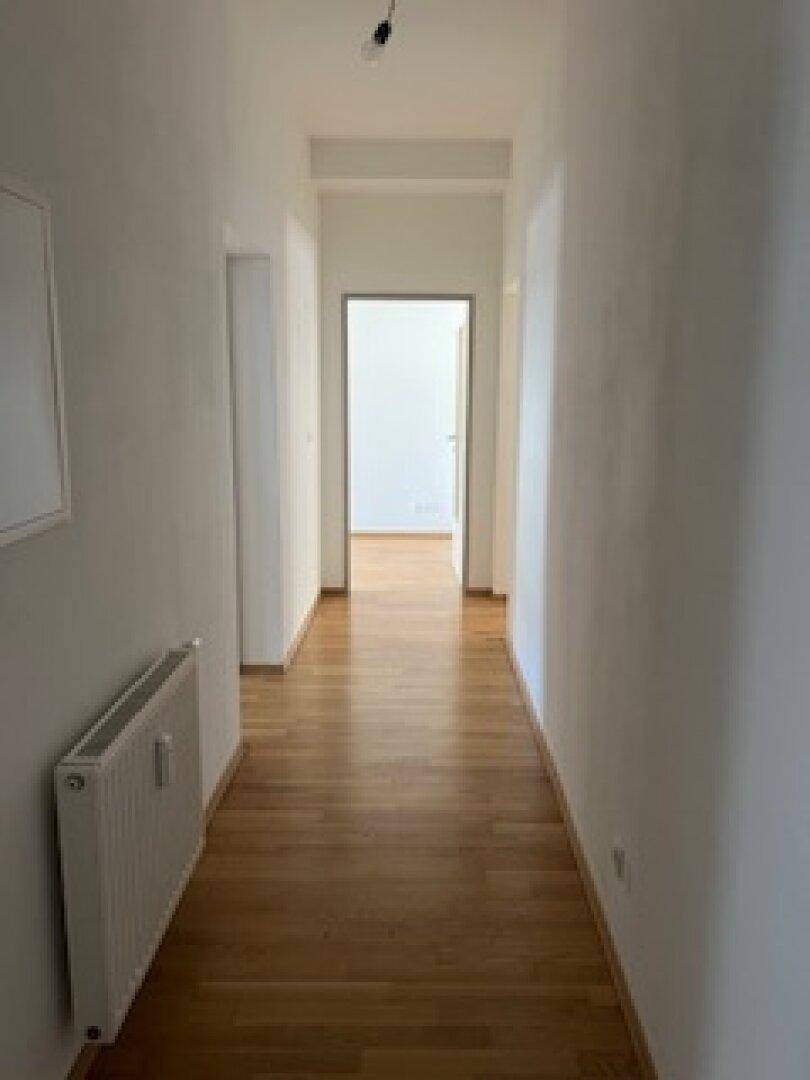 Langer, heller Flur mit Holzboden und weißen Wänden, der die Räume verbindet.