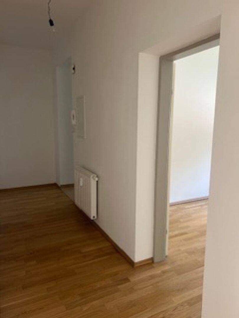 Heller Flur mit Holzboden und weißen Wänden, der zu weiteren Räumen führt.