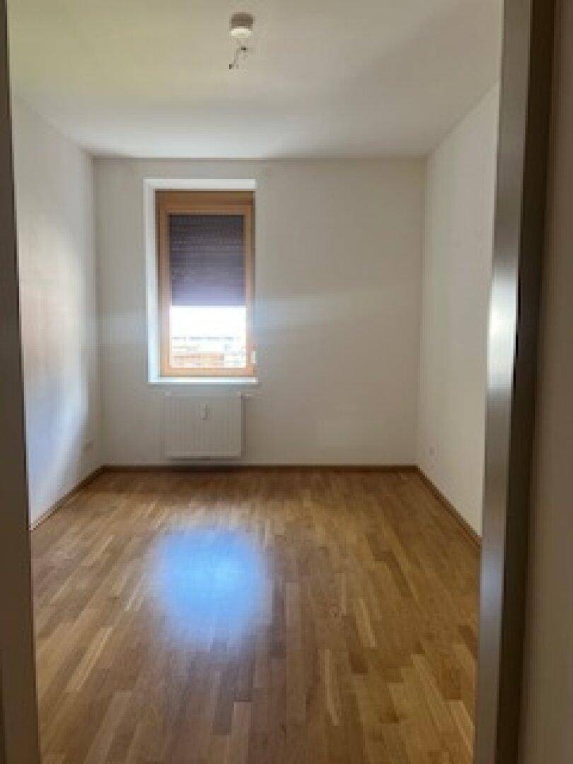 Helles Zimmer mit Holzboden und einem Fenster, das viel natürliches Licht hereinlässt.