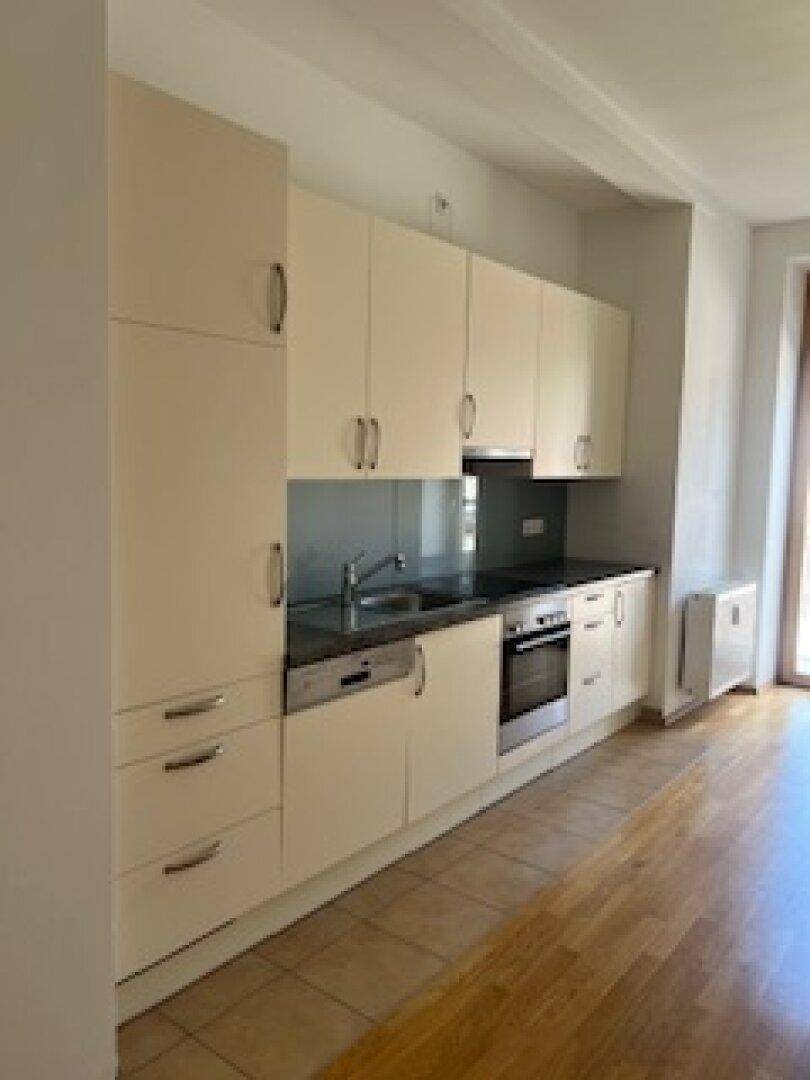 Moderne Einbauküche mit hellen Schränken, dunkler Arbeitsplatte und integrierten Geräten.
