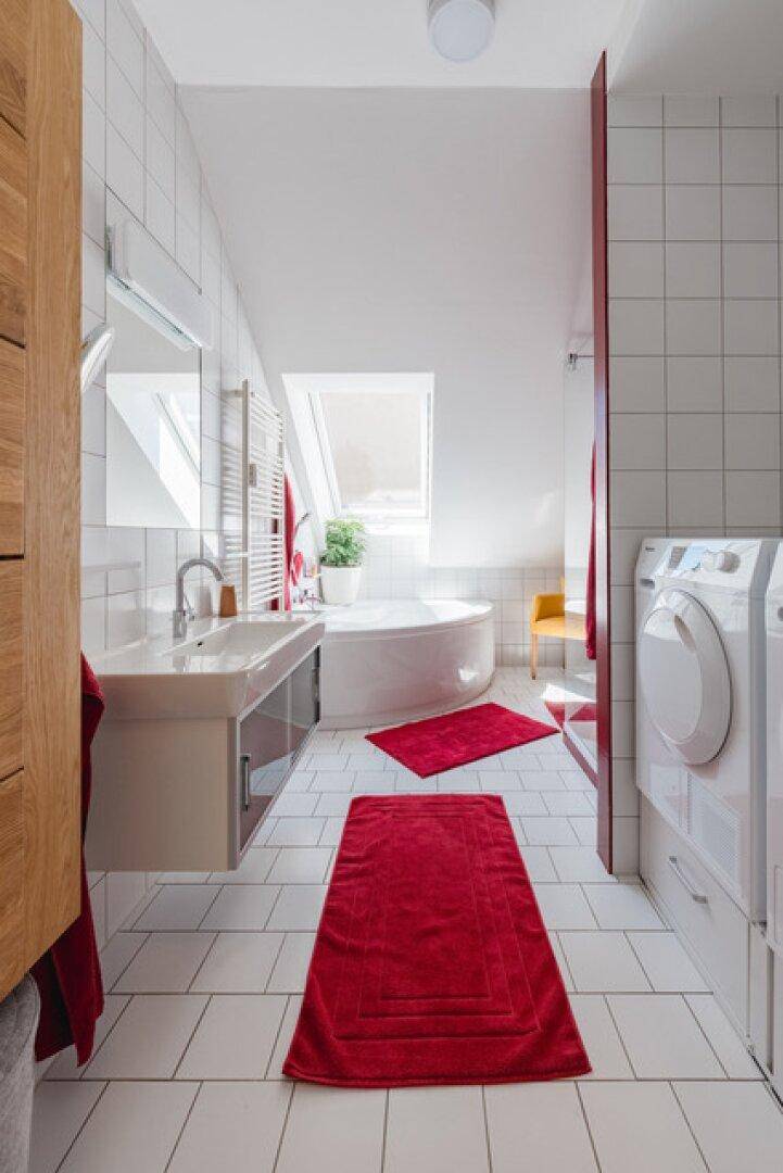 Helles Badezimmer mit Badewanne, Waschmaschine und Dachfenster.