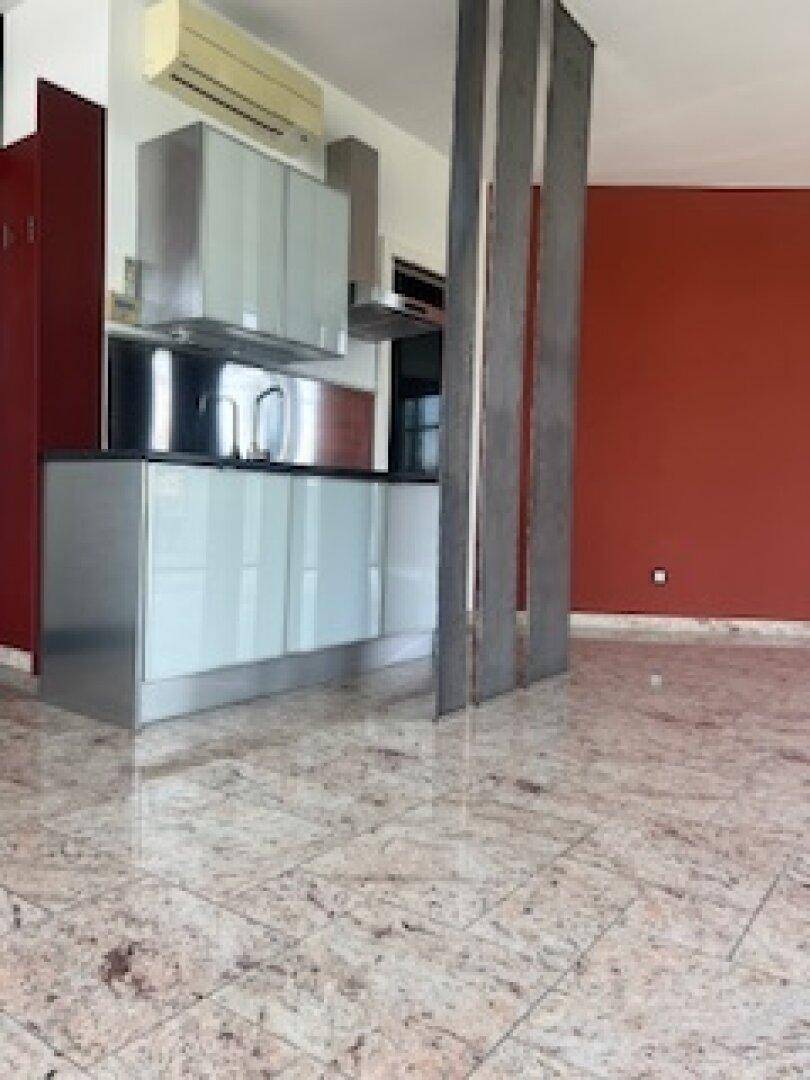 Moderne Küchenzeile mit glänzenden Fronten und roter Wand, integriert in einen offenen Wohnbereich.