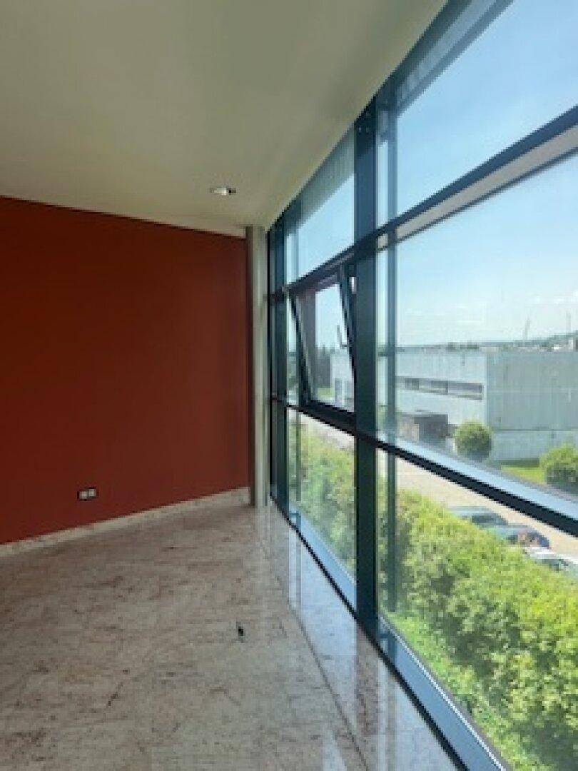 Langer Wohnbereich mit roter Wand und großen Fenstern, die einen Blick auf die Umgebung ermöglichen.
