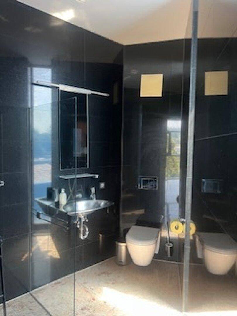 Modernes Badezimmer mit schwarzen Fliesen, wandhängender Toilette und stilvollem Waschbecken.