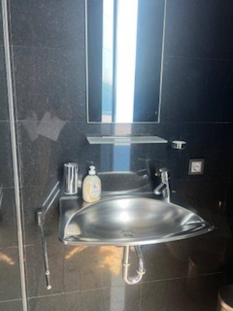 Modernes Waschbecken aus Edelstahl mit Spiegel und Ablage in einem eleganten Badezimmer.
