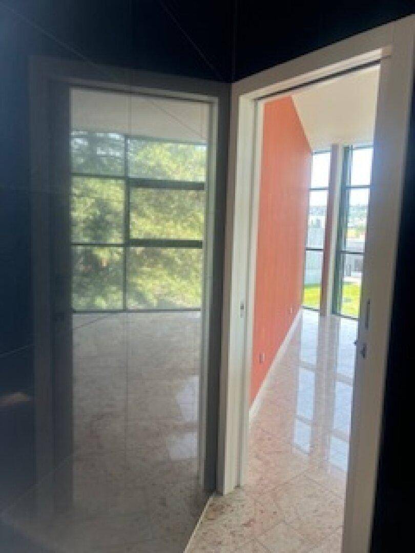 Blick aus dem Badezimmer in einen hellen Flur mit großen Fenstern und roter Akzentwand.