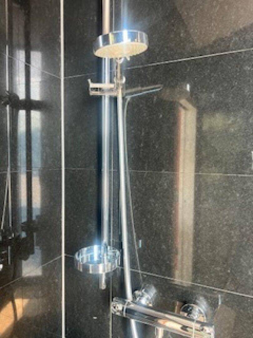 Moderne Duscharmatur mit Regenduschkopf in einem stilvollen Badezimmer mit schwarzen Fliesen.