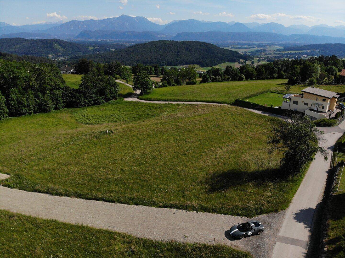 Luftaufnahme eines weitläufigen Grundstücks mit Zufahrtsstraße und beeindruckendem Bergblick in der Ferne.
