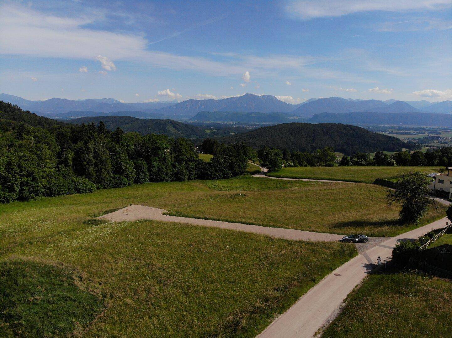 Grundstück mit Zufahrtsstraße und weitem Blick über die grüne Landschaft und die fernen Berge.