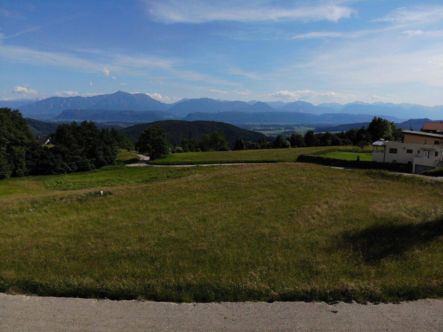 Panoramablick über ein Grundstück mit grüner Landschaft und einem beeindruckenden Bergpanorama am Horizont.