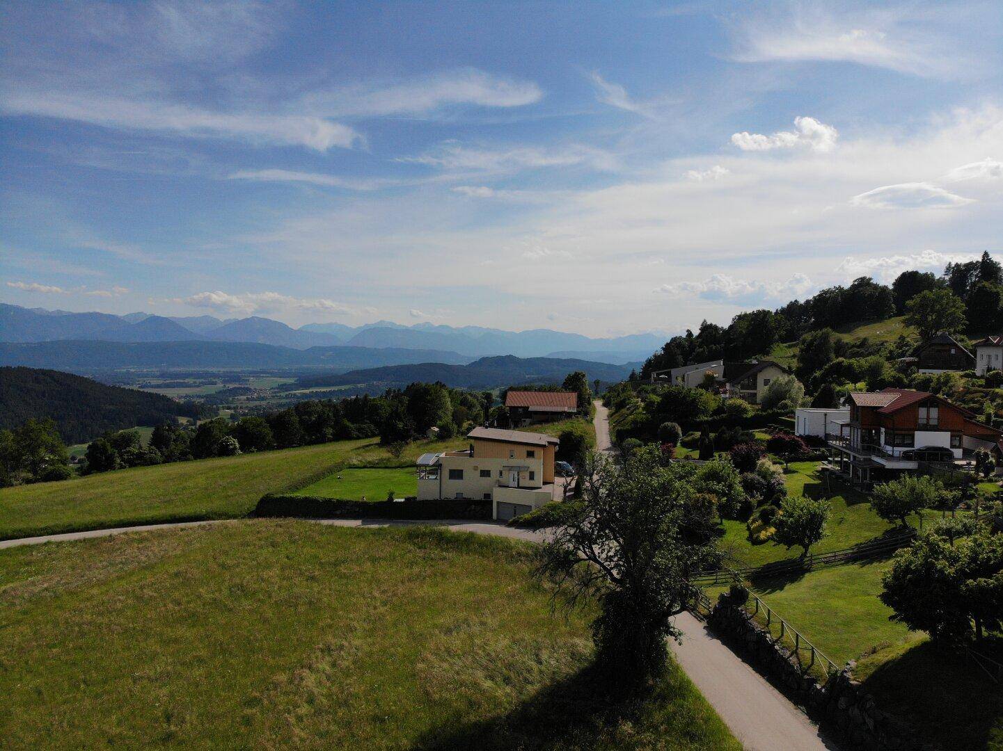 Luftaufnahme eines Grundstücks in Hanglage mit Blick auf umliegende Häuser und die Bergkette.