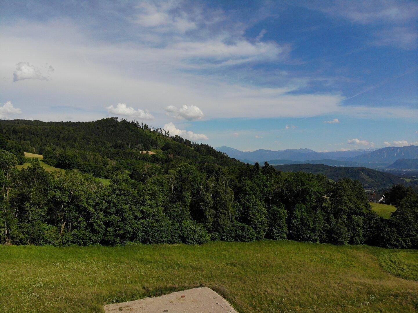 Grundstück mit Zufahrtsweg und weitem Blick über die grüne Landschaft und die fernen Berge.