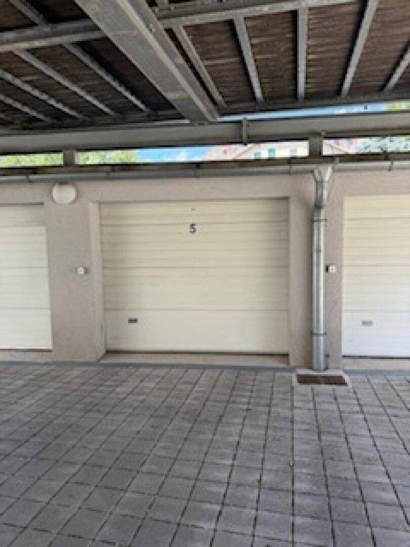 Eine einzelne Garage mit weißem Tor und gepflastertem Zugang, Teil einer größeren Garagenanlage.