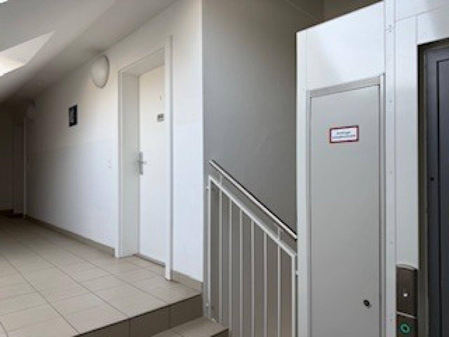Heller Flur mit modernem Aufzug und Treppenhaus, ausgestattet mit Fliesenboden.