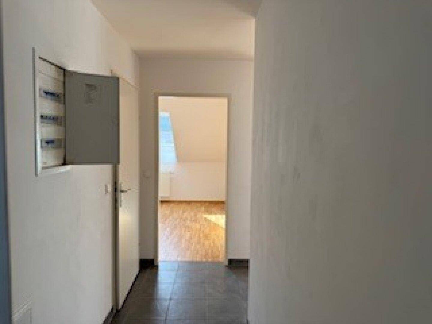 Schlichter Flur mit dunklen Fliesen und weiß gestrichenen Wänden, führt zu einem weiteren Raum.