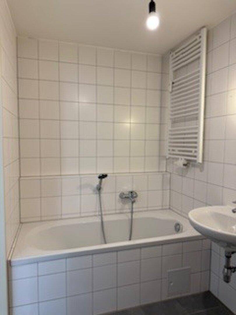 Badezimmer mit weißen Fliesen, Badewanne, Waschbecken und einem praktischen Handtuchheizkörper.