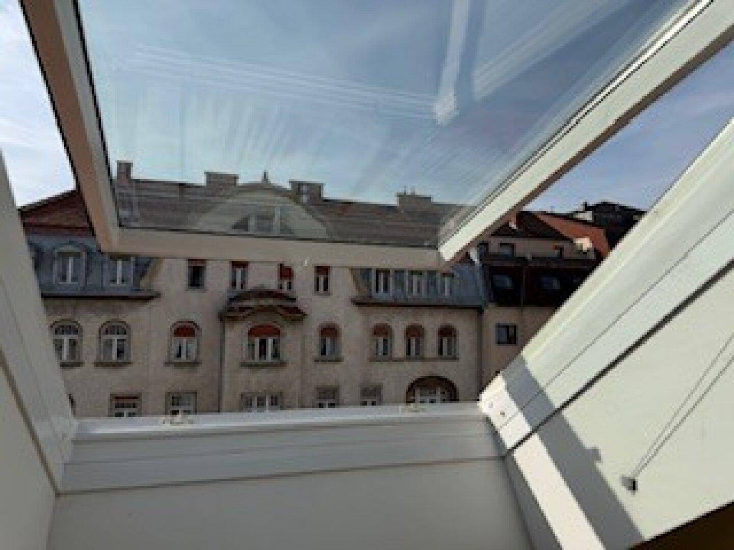 Blick aus einem Dachfenster auf eine historische Gebäudefassade mit zahlreichen Fenstern und Details.