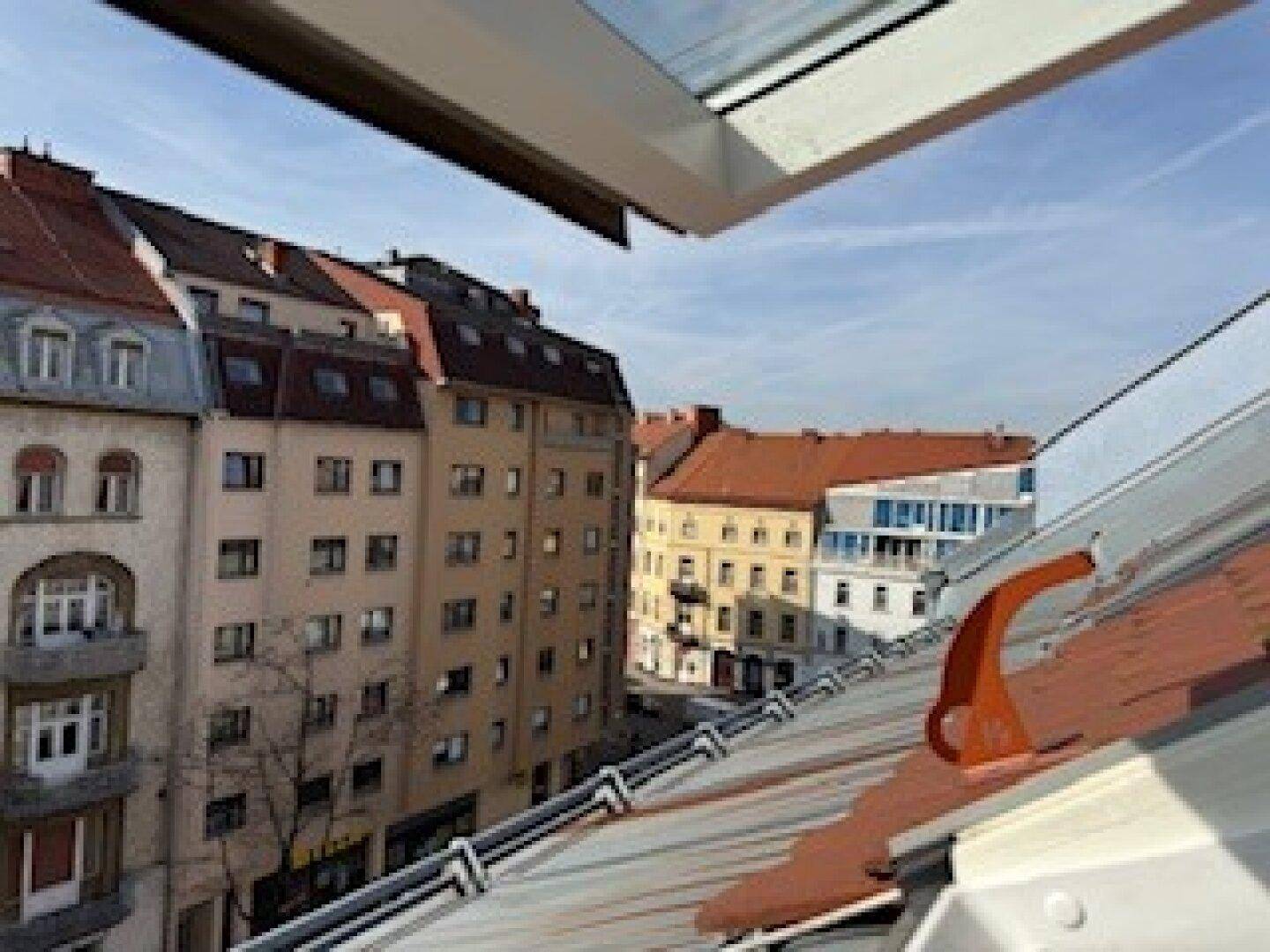 Weitblick über eine städtische Straße mit verschiedenen Gebäuden und Dächern unter blauem Himmel.