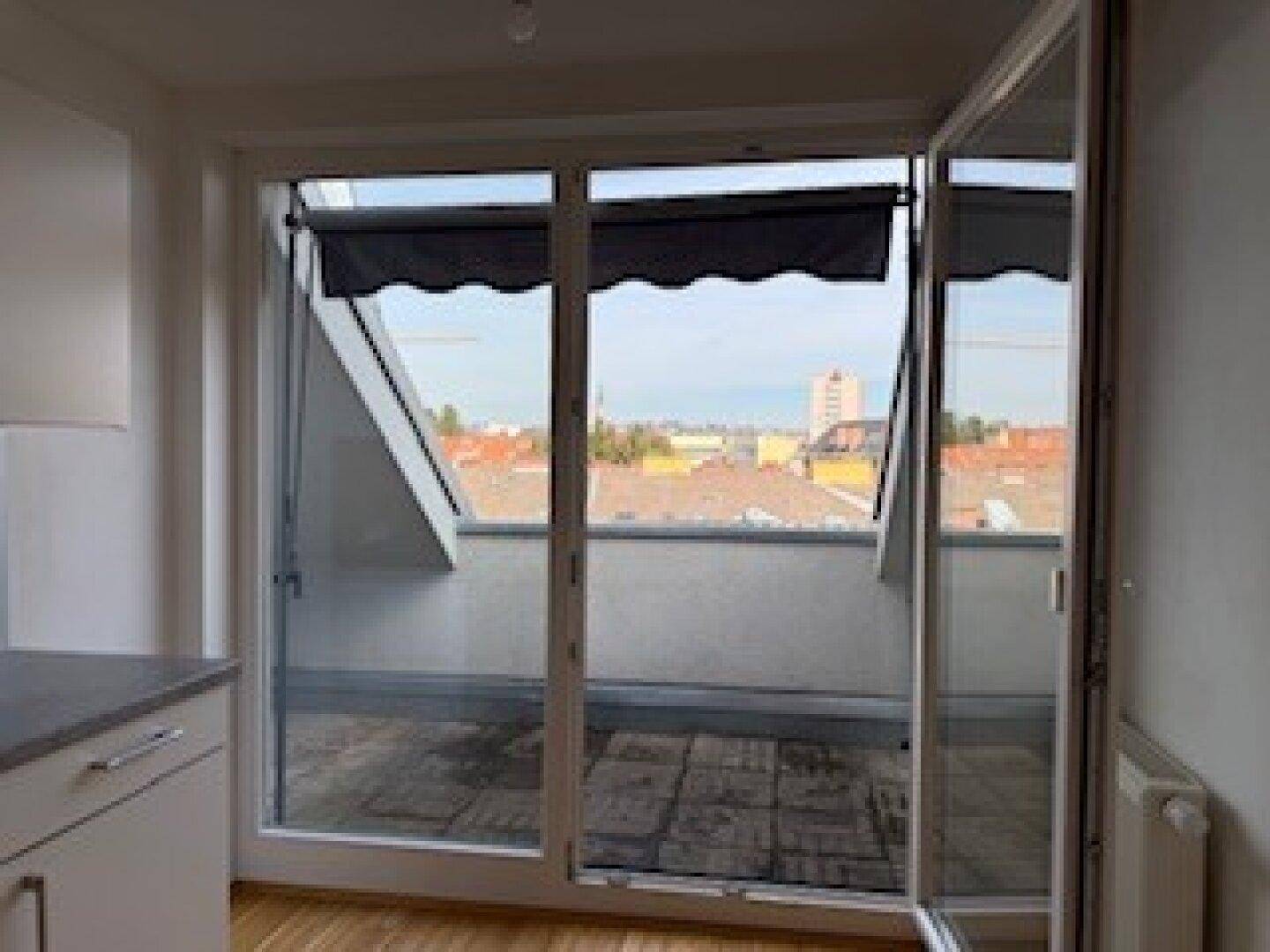 Große Glastür führt zu einem Balkon mit Blick über die Dächer der Stadt.