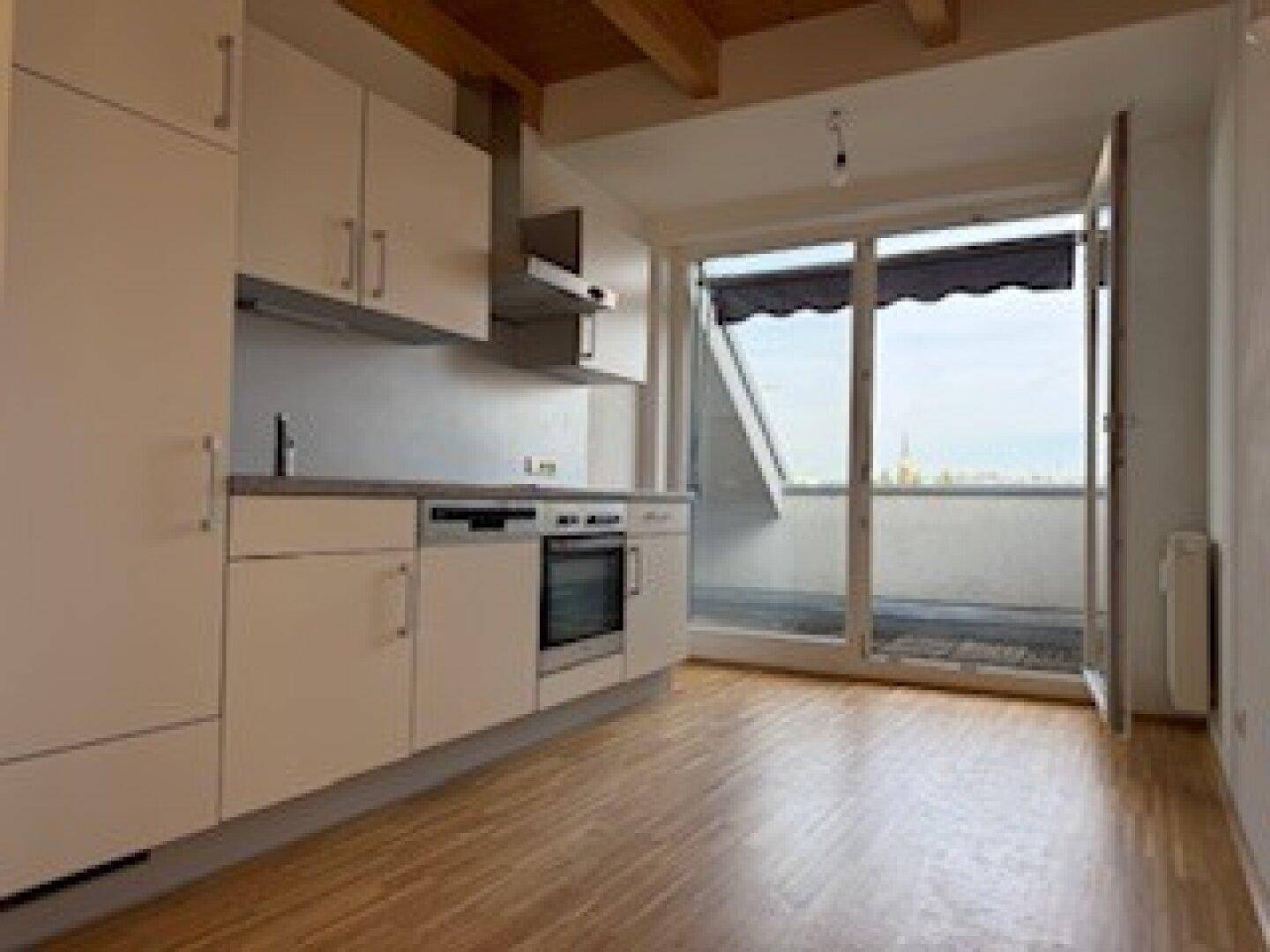Helle Küchenzeile mit Holzboden und Zugang zu einem Balkon, unter sichtbaren Holzdeckenbalken.