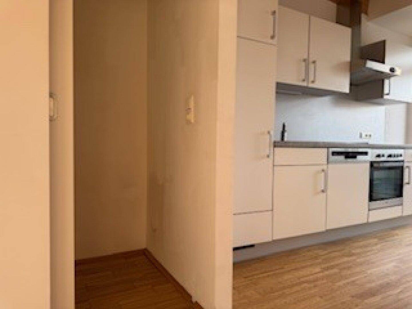Kompakte Küchenzeile mit hellen Schränken und angrenzendem Abstellbereich, ausgestattet mit Holzboden.