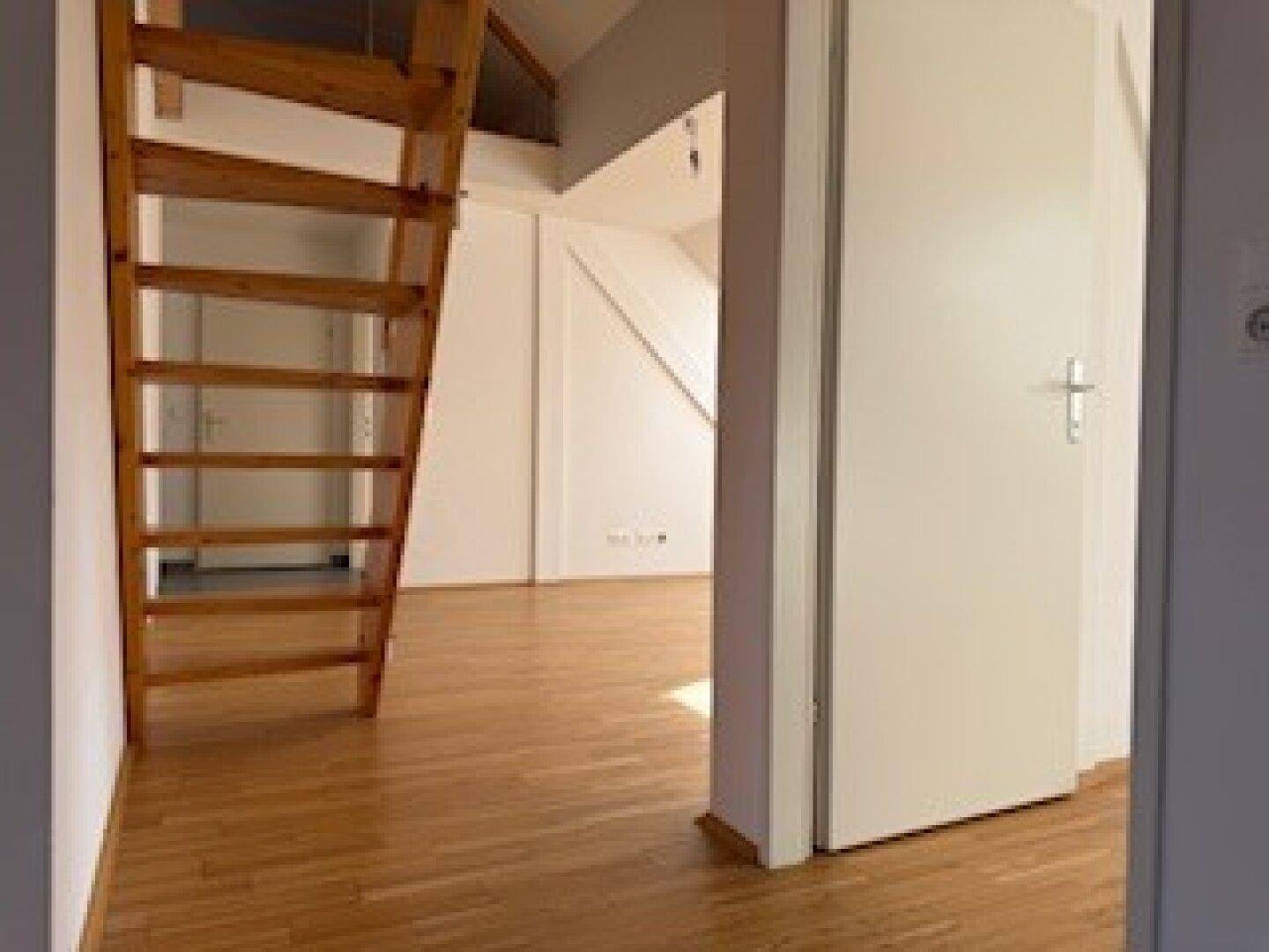 Offener Wohnbereich mit Holzboden und einer Holztreppe, die zu einer oberen Ebene führt.