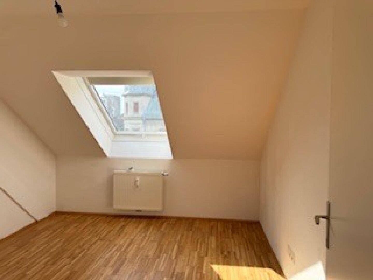 Gemütliches Zimmer mit Holzboden, Dachschräge und einem Dachfenster, das den Raum erhellt.