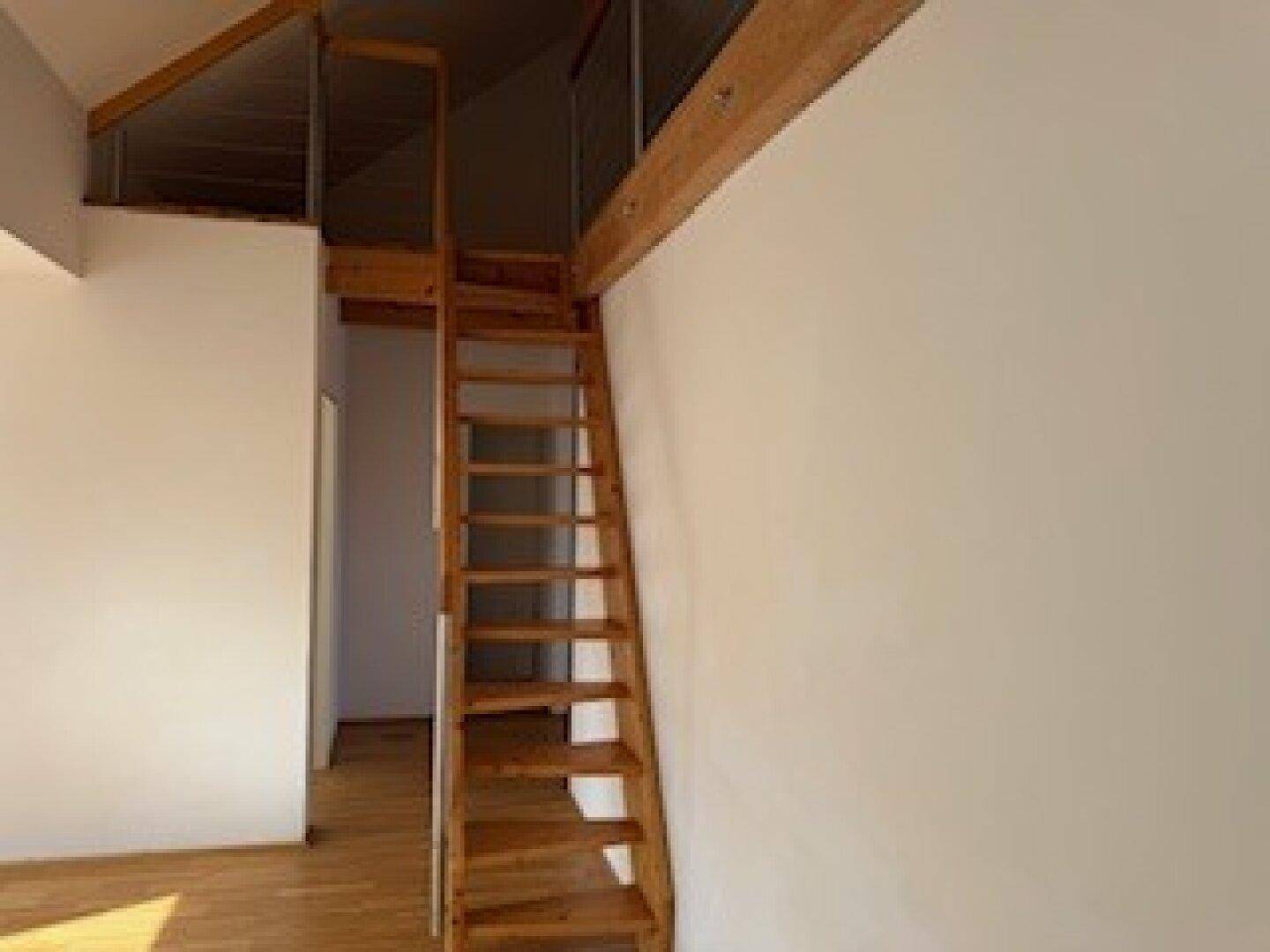 Geräumiger Wohnbereich mit Holzboden, Dachschrägen und einer Holztreppe, die nach oben führt.
