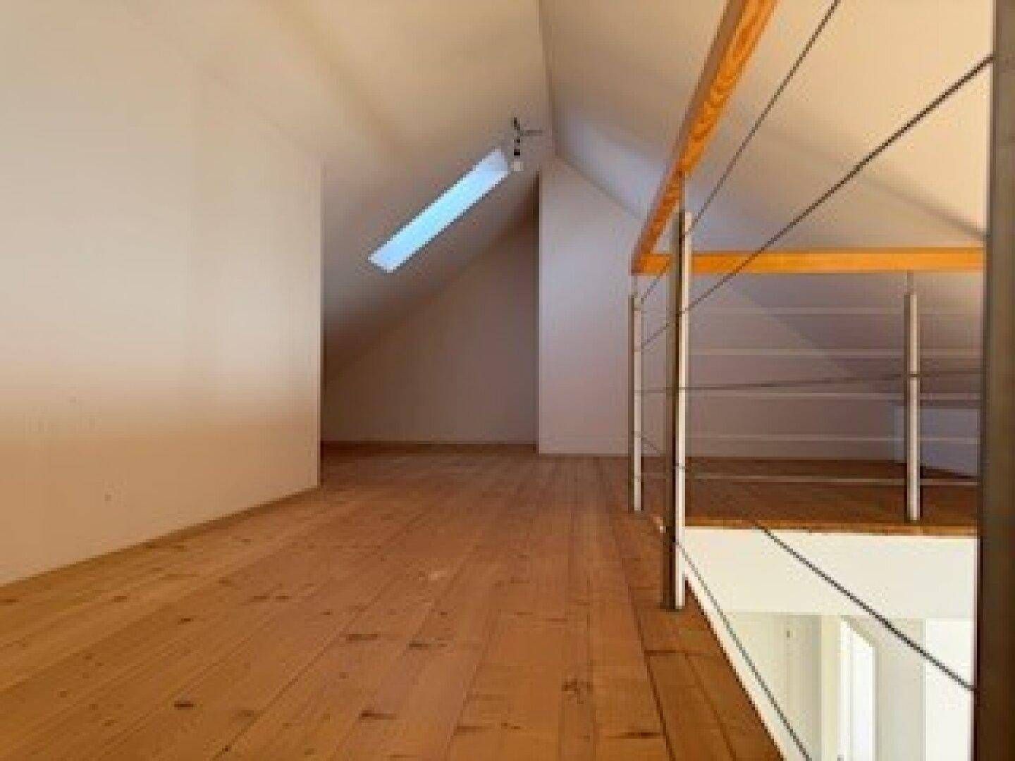 Geräumiger Dachbodenbereich mit Holzdielenboden, schrägen Wänden und einem Dachfenster.