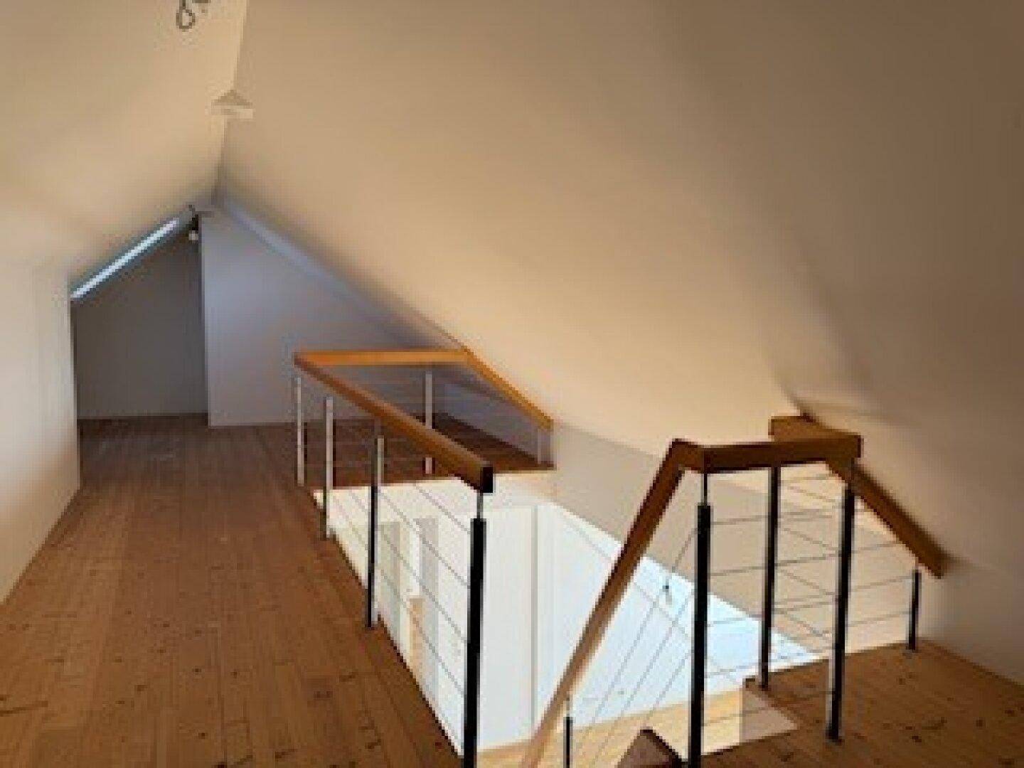 Blick vom Dachgeschoss auf die Treppe zum unteren Bereich mit Holzboden und modernem Geländer.