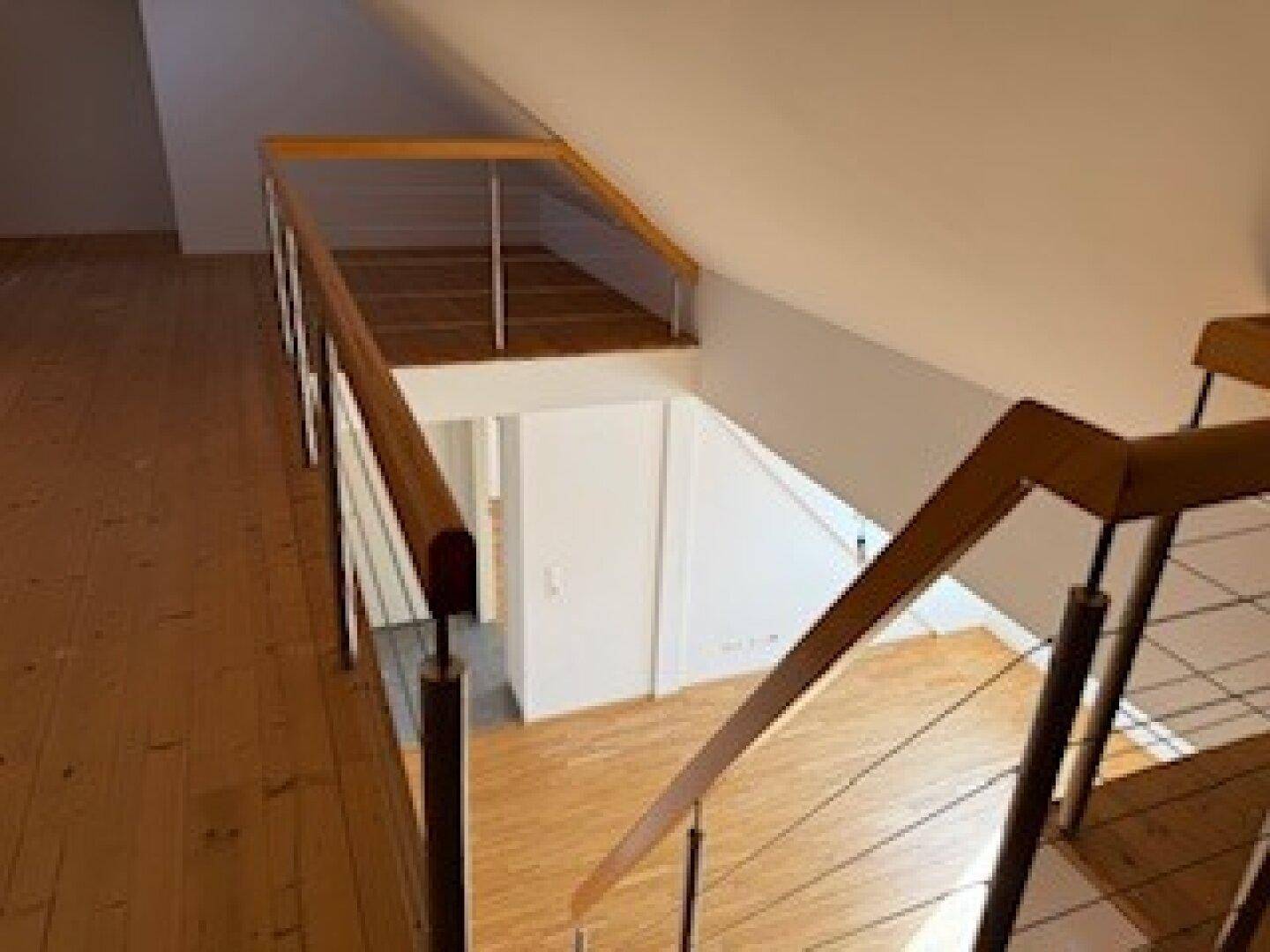 Dachgeschoss mit Blick auf die Treppe und den darunterliegenden Flur mit weißer Tür.
