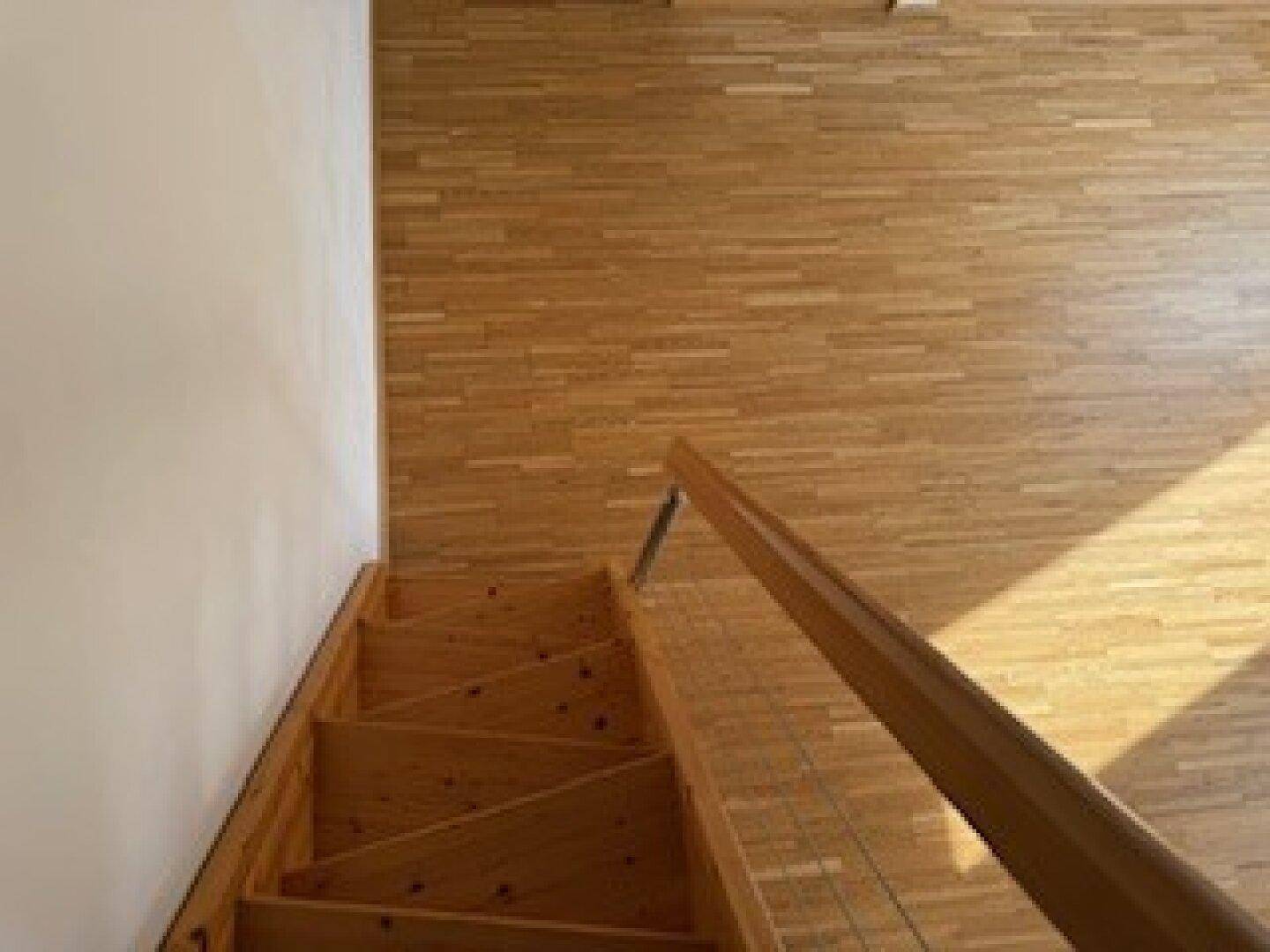 Holztreppe führt nach unten, umgeben von hellem Holzdielenboden.