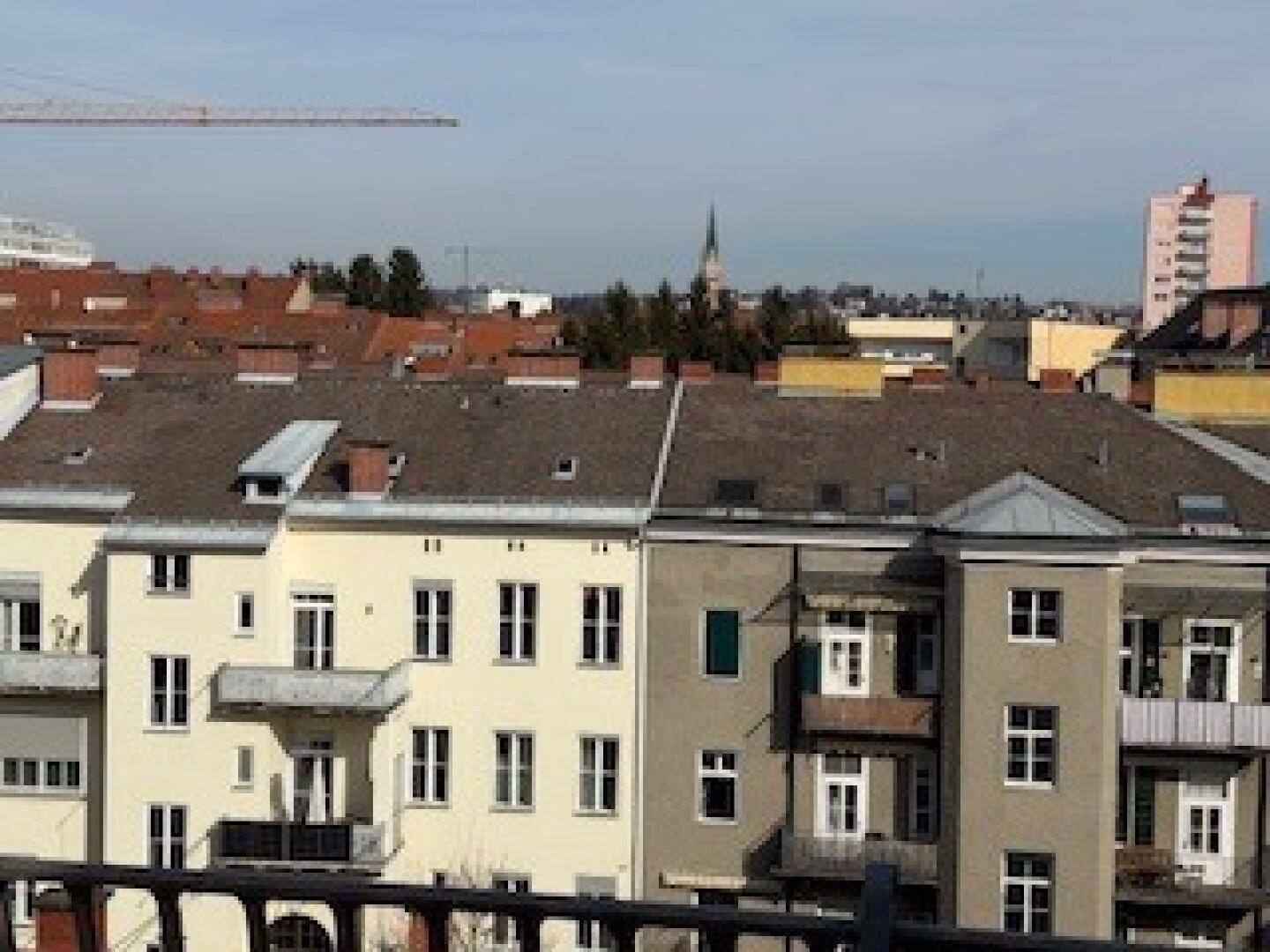 Weitblick über die städtische Dachlandschaft mit historischen Gebäuden und einem Kirchturm.