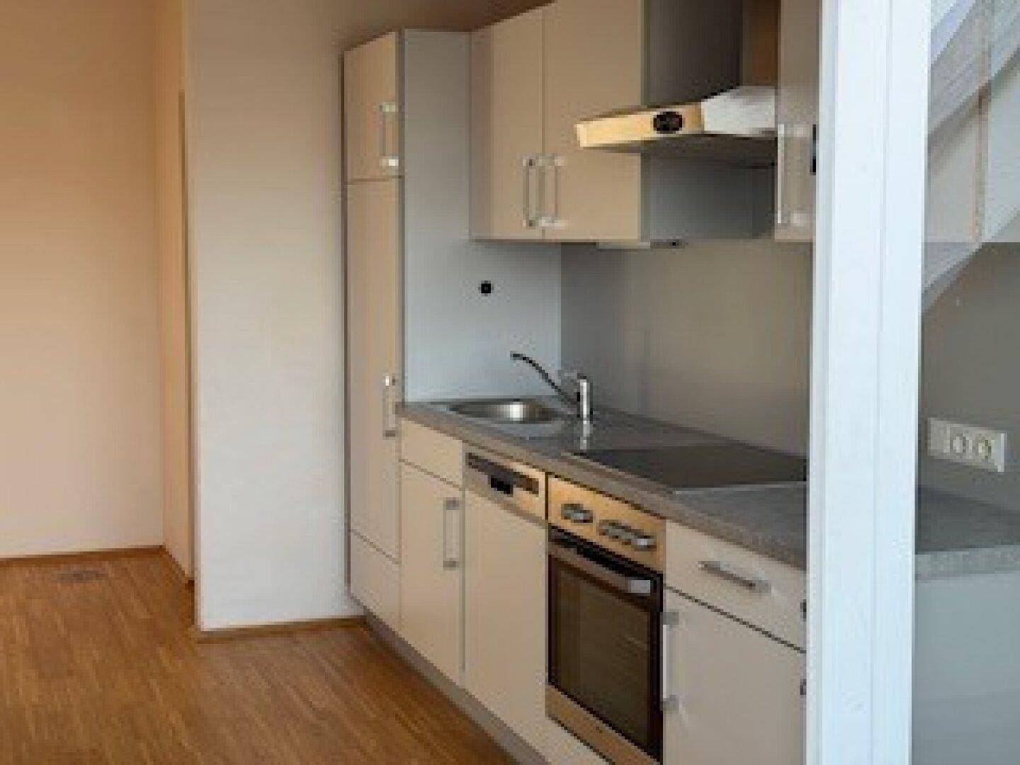 Funktionale Küchenzeile mit hellen Schränken, integrierten Geräten und Holzfußboden in einem modernen Raum.