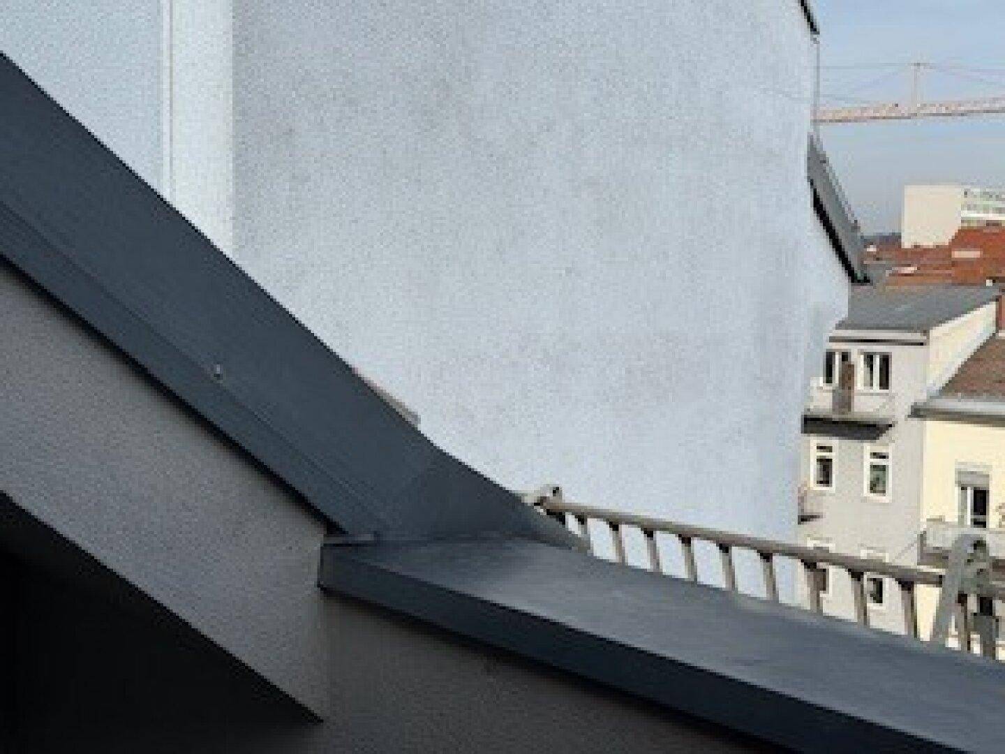 Ansicht einer modernen Gebäudefassade mit grauer Wand und einem dunklen, schrägen Dach.