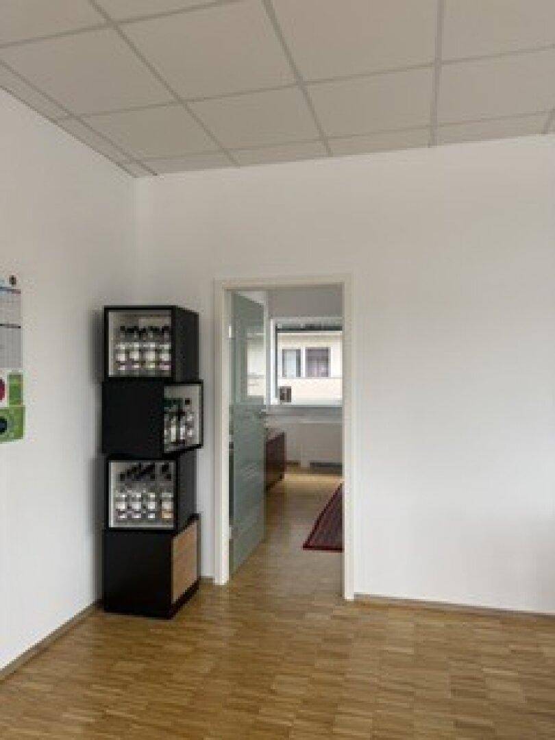 Flur mit Holzparkettboden und Blick in einen weiteren Büroraum durch eine moderne Glastür.
