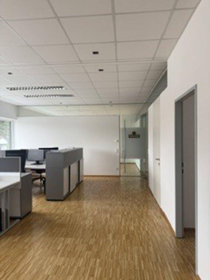 Langer Bürogang mit Holzparkettboden und modernen Arbeitsplätzen auf der linken Seite des Raumes.