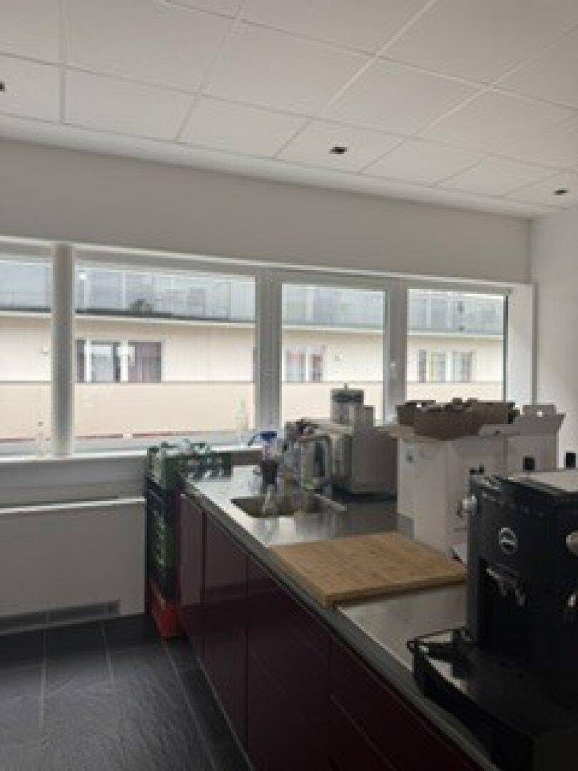 Küchenzeile mit Spüle, Kaffeemaschine und Blick auf ein gegenüberliegendes Gebäude durch die Fenster.