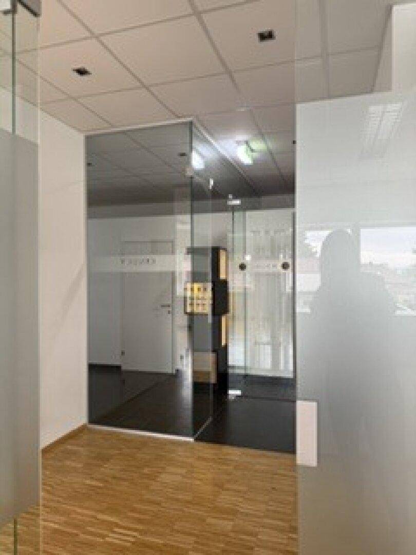 Moderner Eingangsbereich mit Glaswänden, Holzparkett und dunklem Fliesenboden, der Eleganz verleiht.