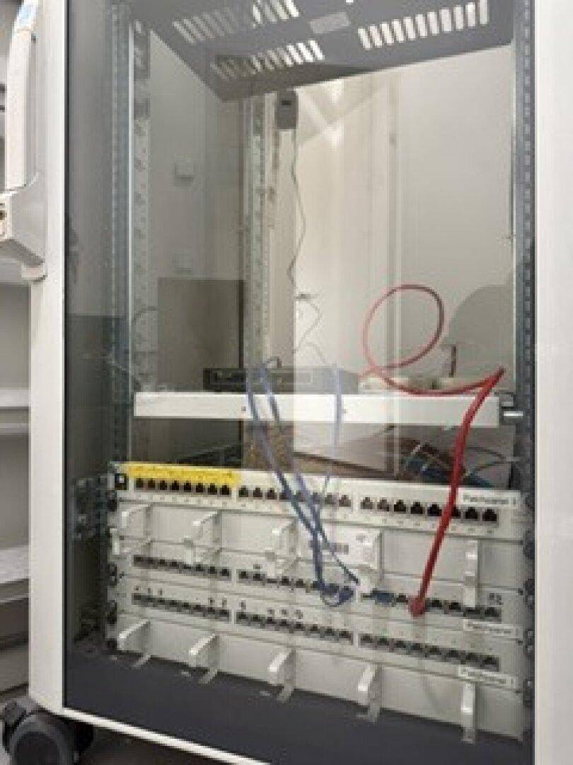 Serverschrank mit Verkabelung und Netzwerkgeräten in einem Technikraum für die IT-Infrastruktur.