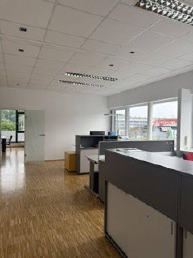 Geräumiges Büro mit Holzparkettboden, großen Fenstern und modernen Arbeitsplätzen in heller Umgebung.