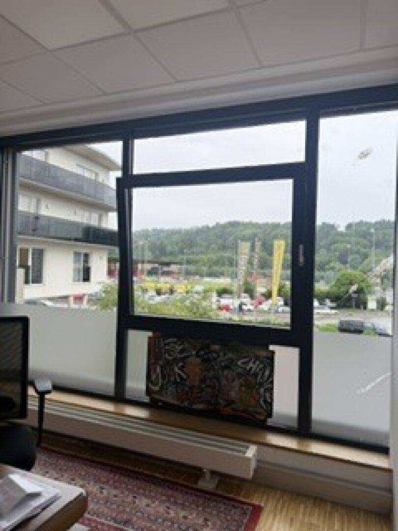 Blick aus einem Bürofenster mit weitem Ausblick auf eine Straße, Parkplätze und bewaldete Hügel.