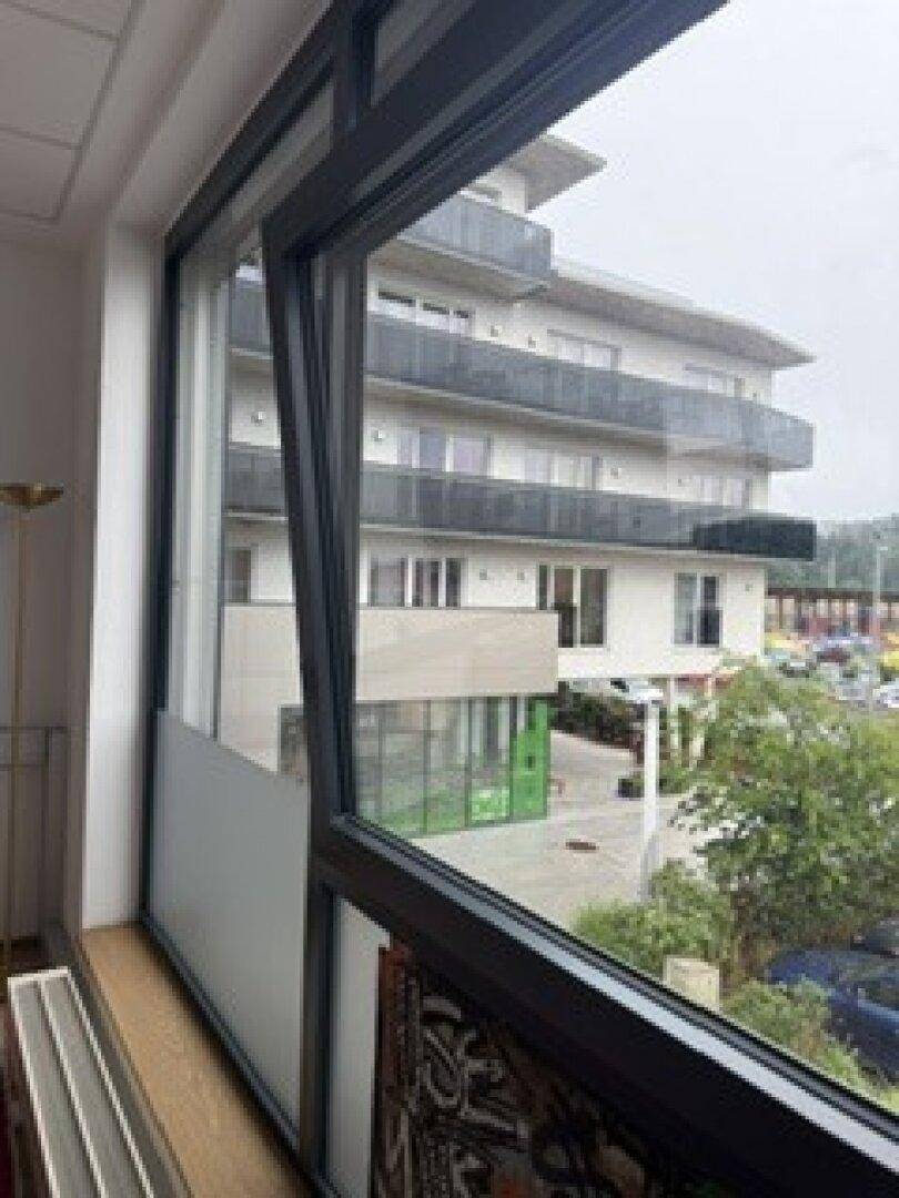 Seitenansicht aus einem Bürofenster, das ein gegenüberliegendes Gebäude und den umliegenden Bereich zeigt.