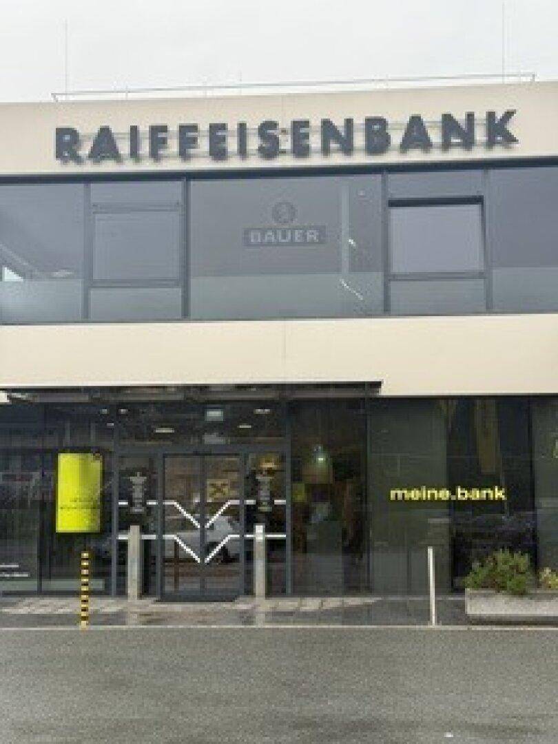 Fassade eines modernen Geschäftsgebäudes mit großen Fenstern und dem Schriftzug "Raiffeisenbank" oben.