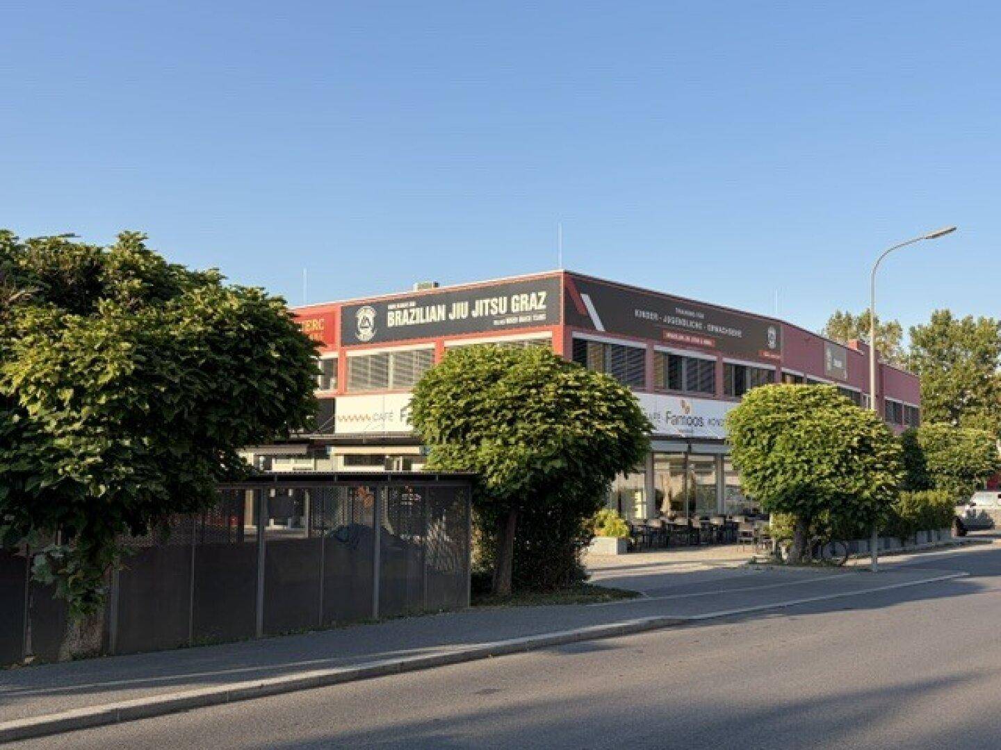 Blick auf das Geschäftsgebäude von der Straßenseite, mit Bäumen im Vordergrund und klarem Himmel.
