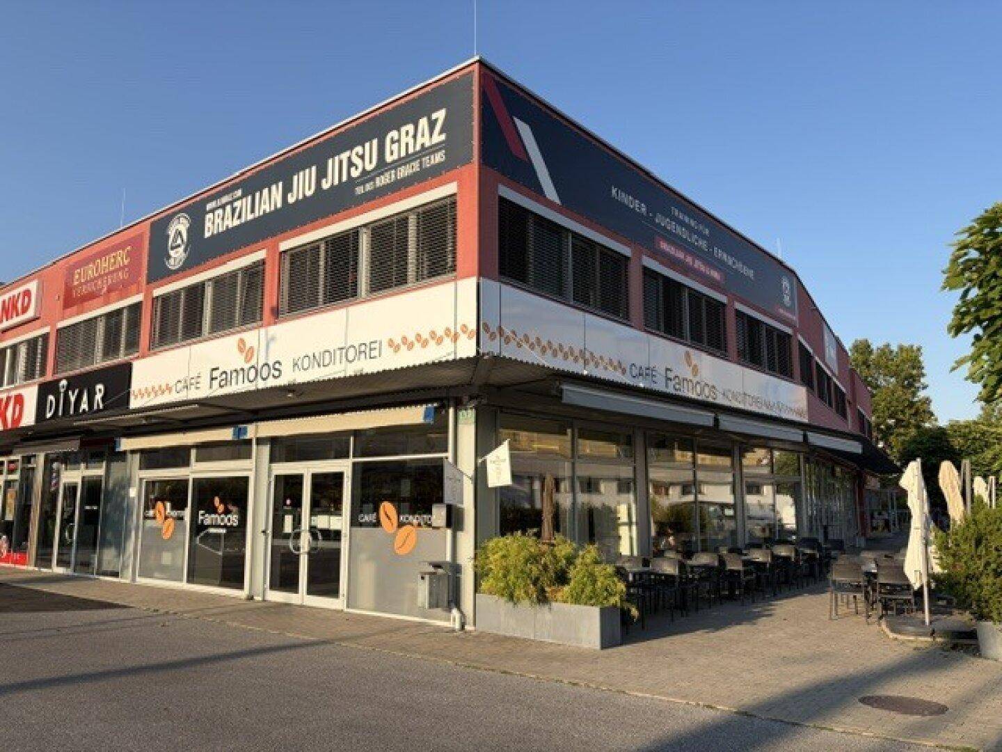 Nahaufnahme der Ecke des Geschäftsgebäudes mit dem Café Famoos und der Kampfsportschule im Obergeschoss.