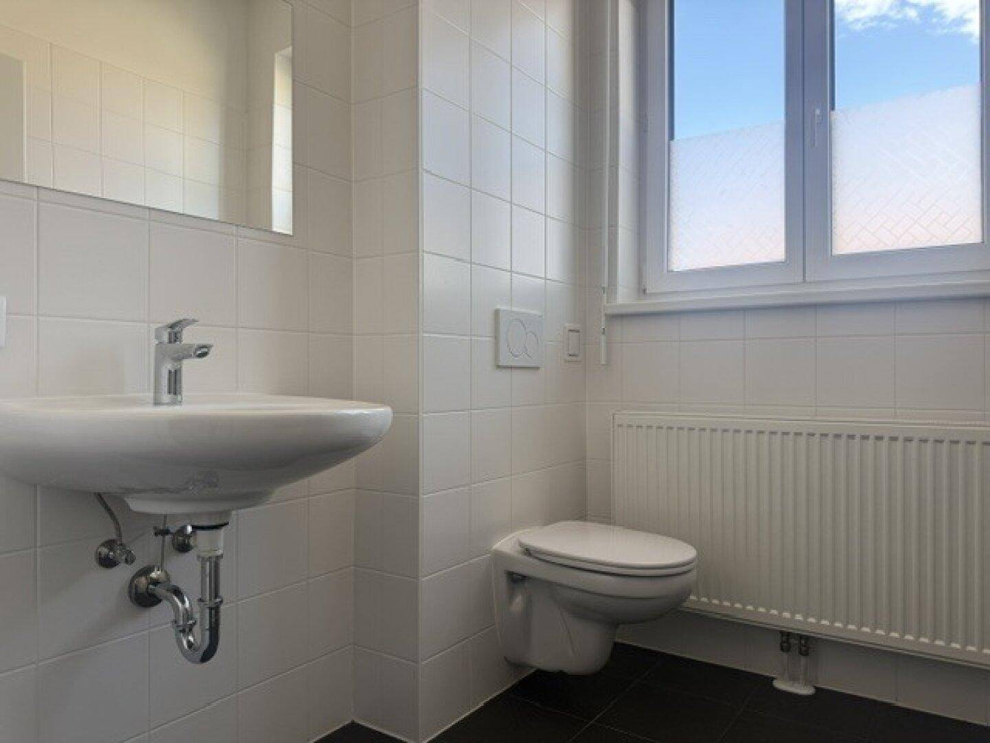 Modernes Badezimmer mit wandhängendem WC, Waschbecken und weiß gefliesten Wänden.