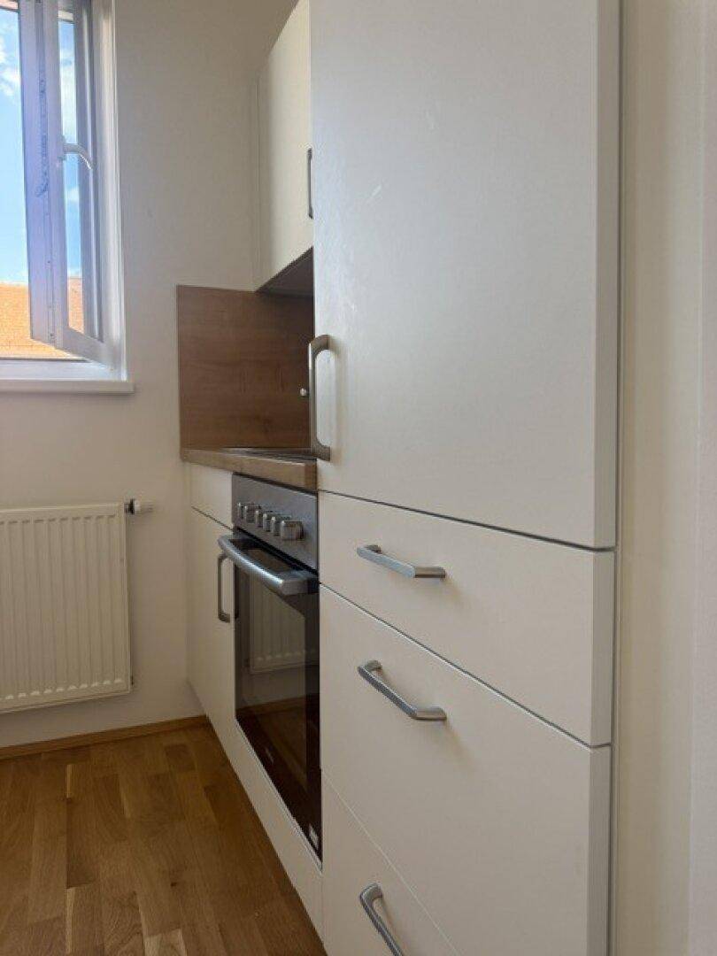 Detailansicht der weißen Einbauküche mit Backofen und Fenster, das Tageslicht hereinlässt.