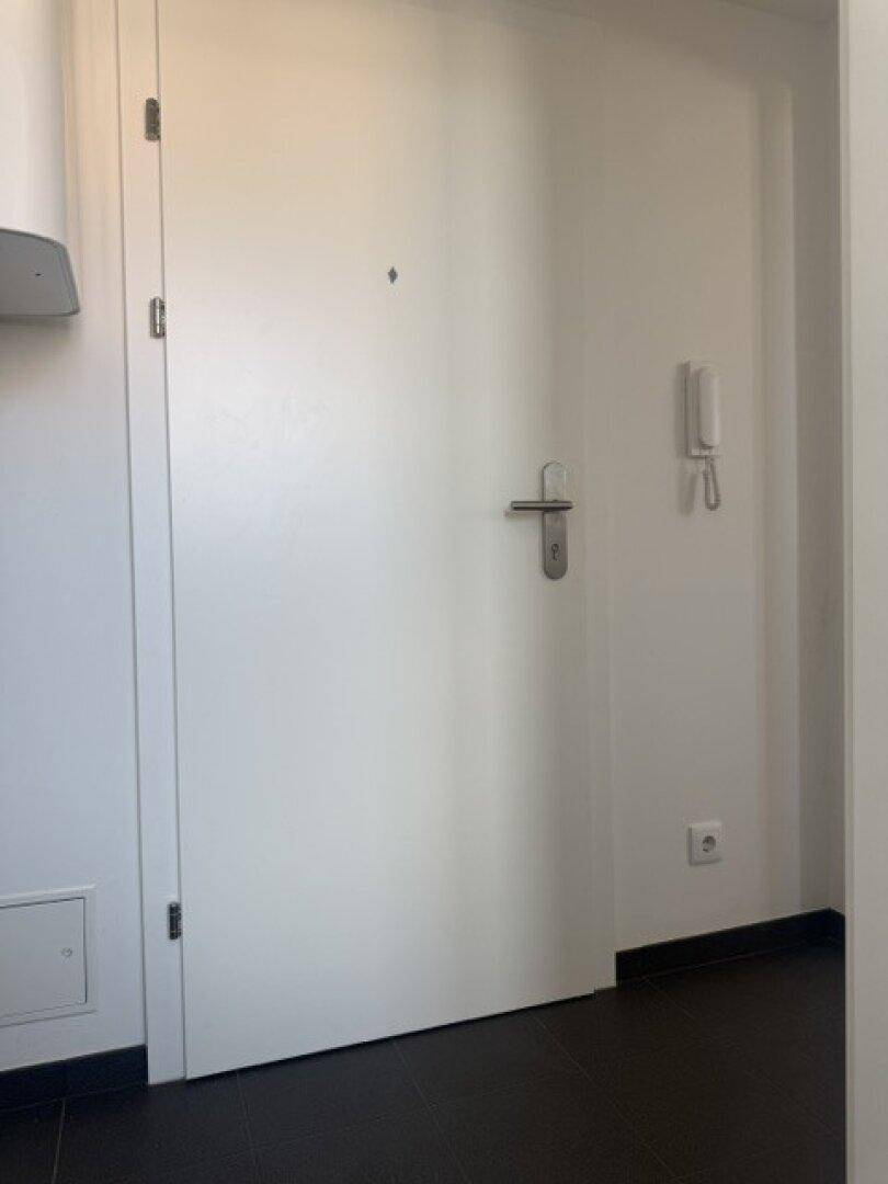 Eingangsbereich mit weißer Wohnungstür, Gegensprechanlage und dunklem Fliesenboden.